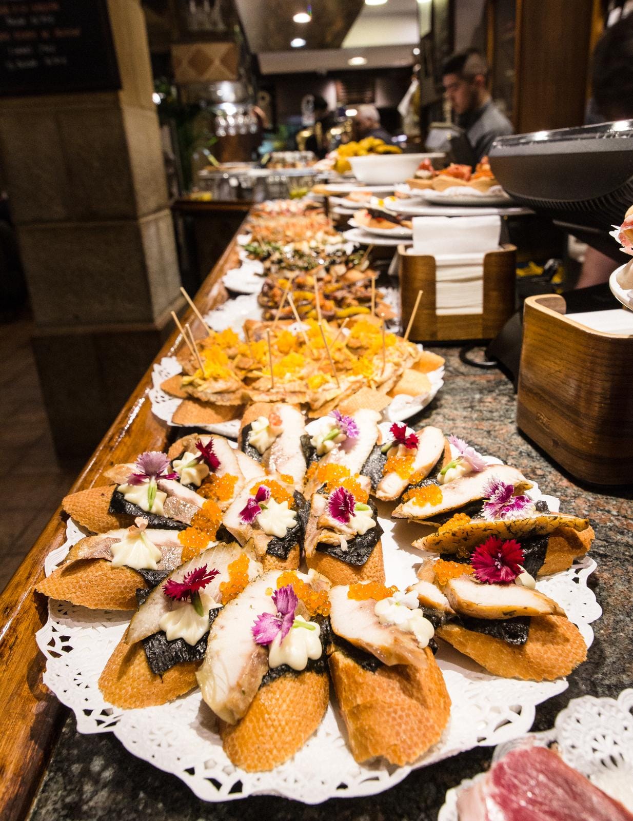 Eine Bar mit spanischen Pintxos auf Tellern, bunt dekoriert mit Blüten.
