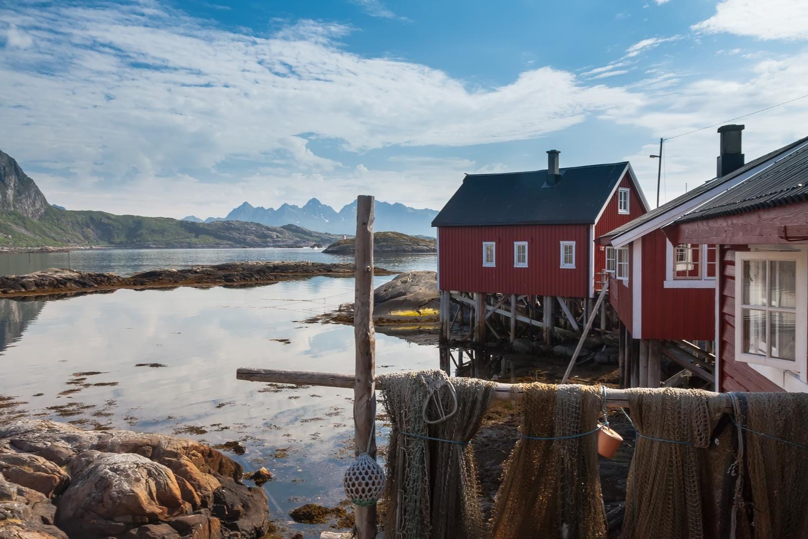 Rote Fischerhütten an Norwegens Küste, ruhiges Wasser, Berge im Hintergrund.