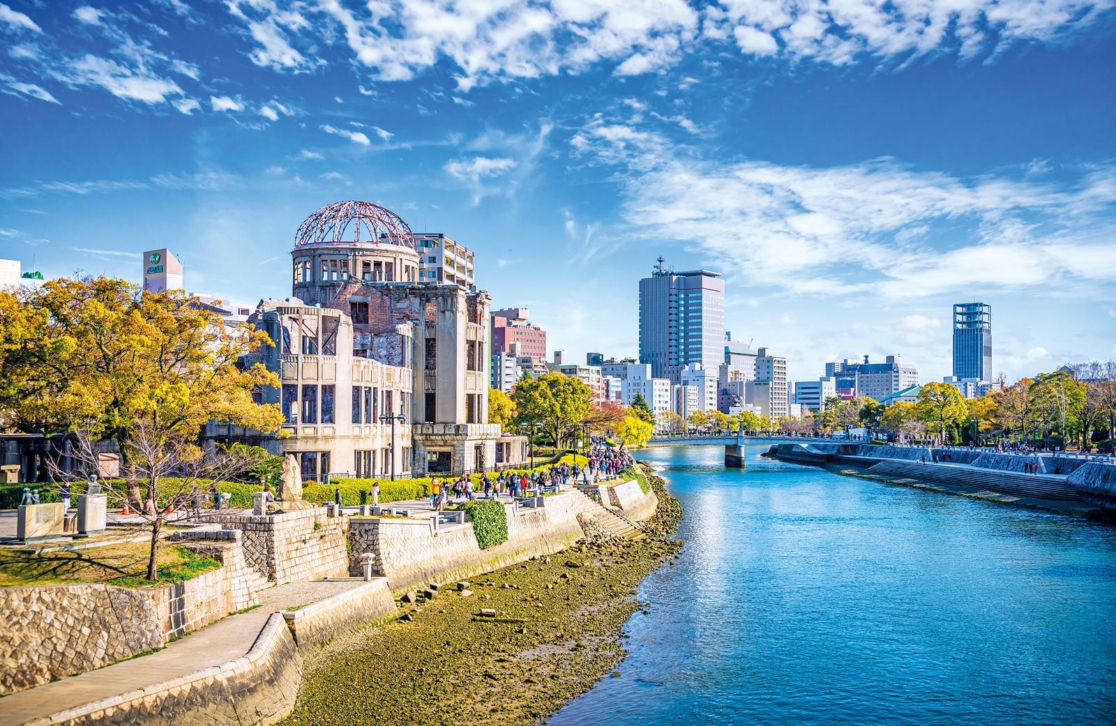 Uferpromenade in Hiroshima, Japan, mit historischem Gebäude und moderner Skyline bei Sonnenschein.