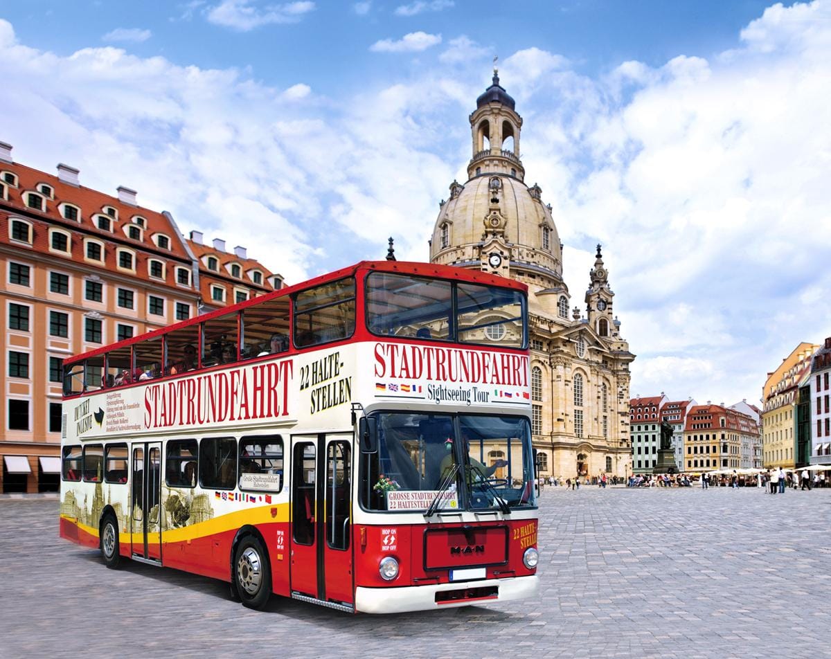 Doppeldecker-Bus vor der Frauenkirche in Dresden, Deutschland, bei blauem Himmel und Sonne.
