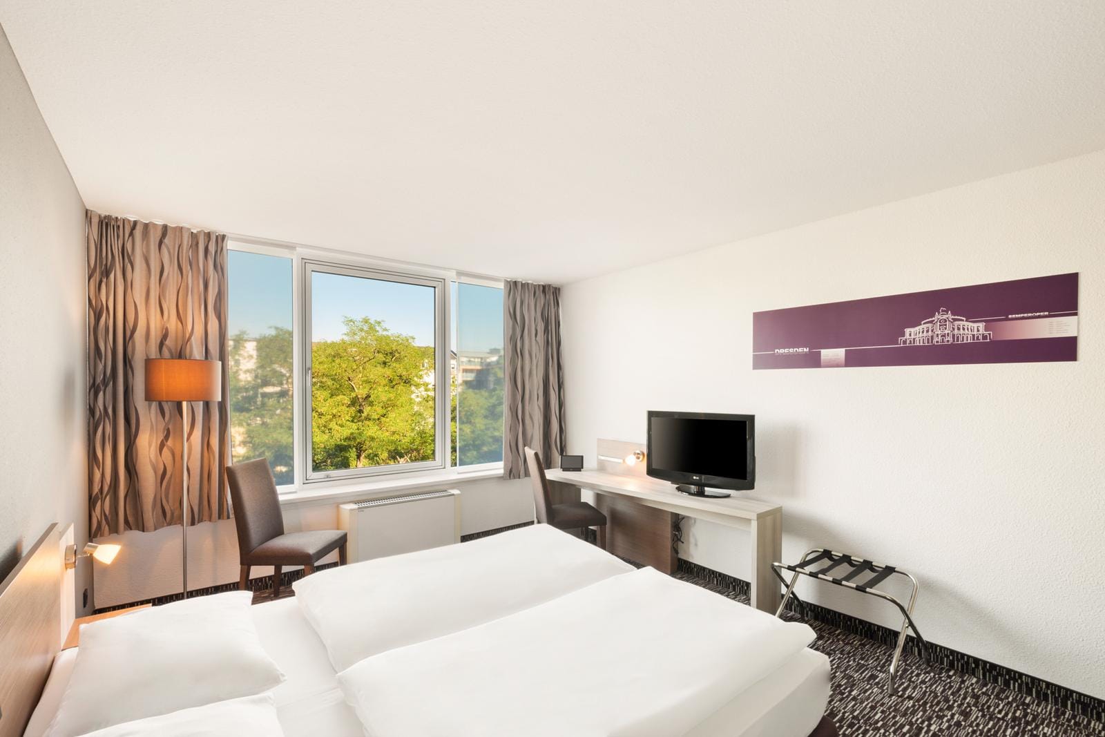 Modernes Hotelzimmer in einer deutschen Stadt mit Blick auf grüne Bäume durch das Fenster.