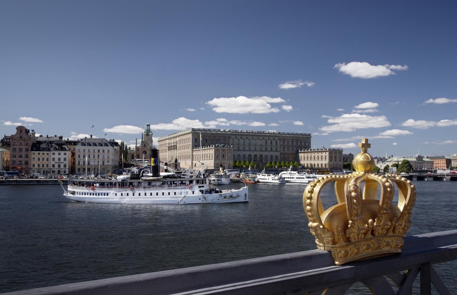 Goldene Krone vor Stockholmer Schloss, blaue Himmel, Boote im Wasser.