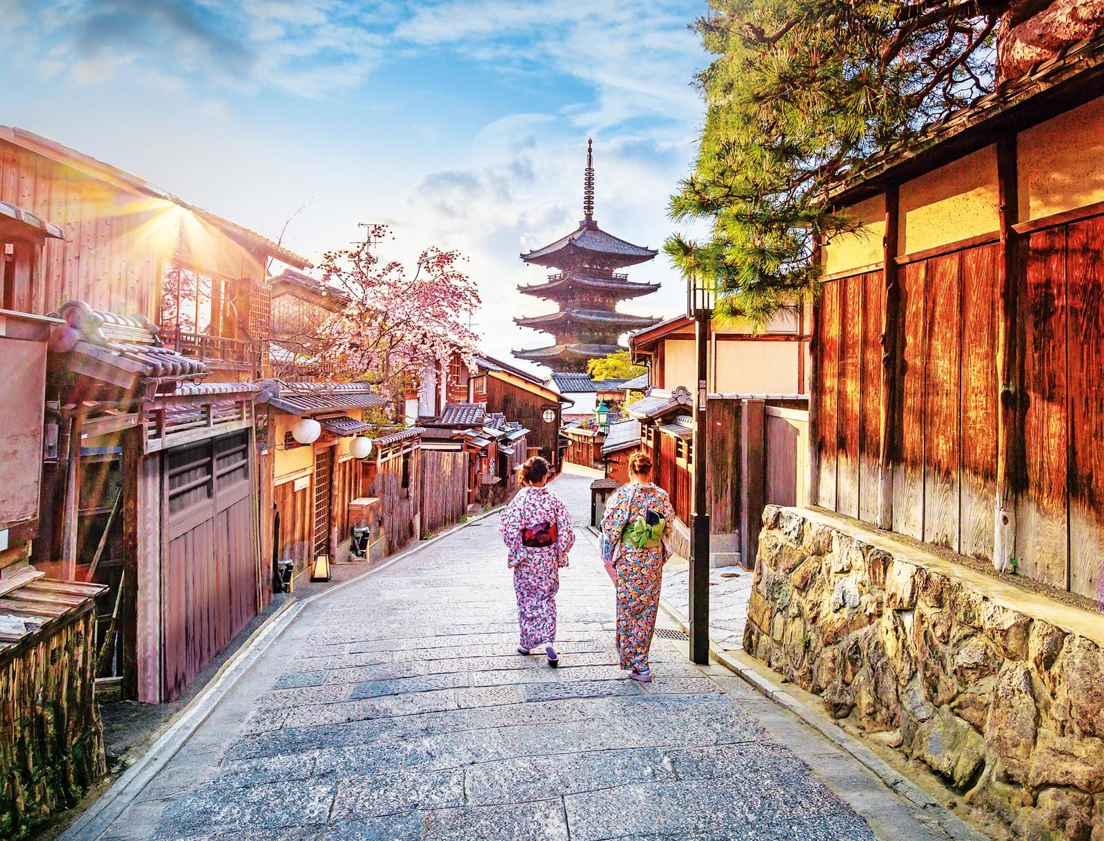 Zwei Frauen in Kimonos schlendern durch Kyotos historische Gassen bei Sonnenschein.