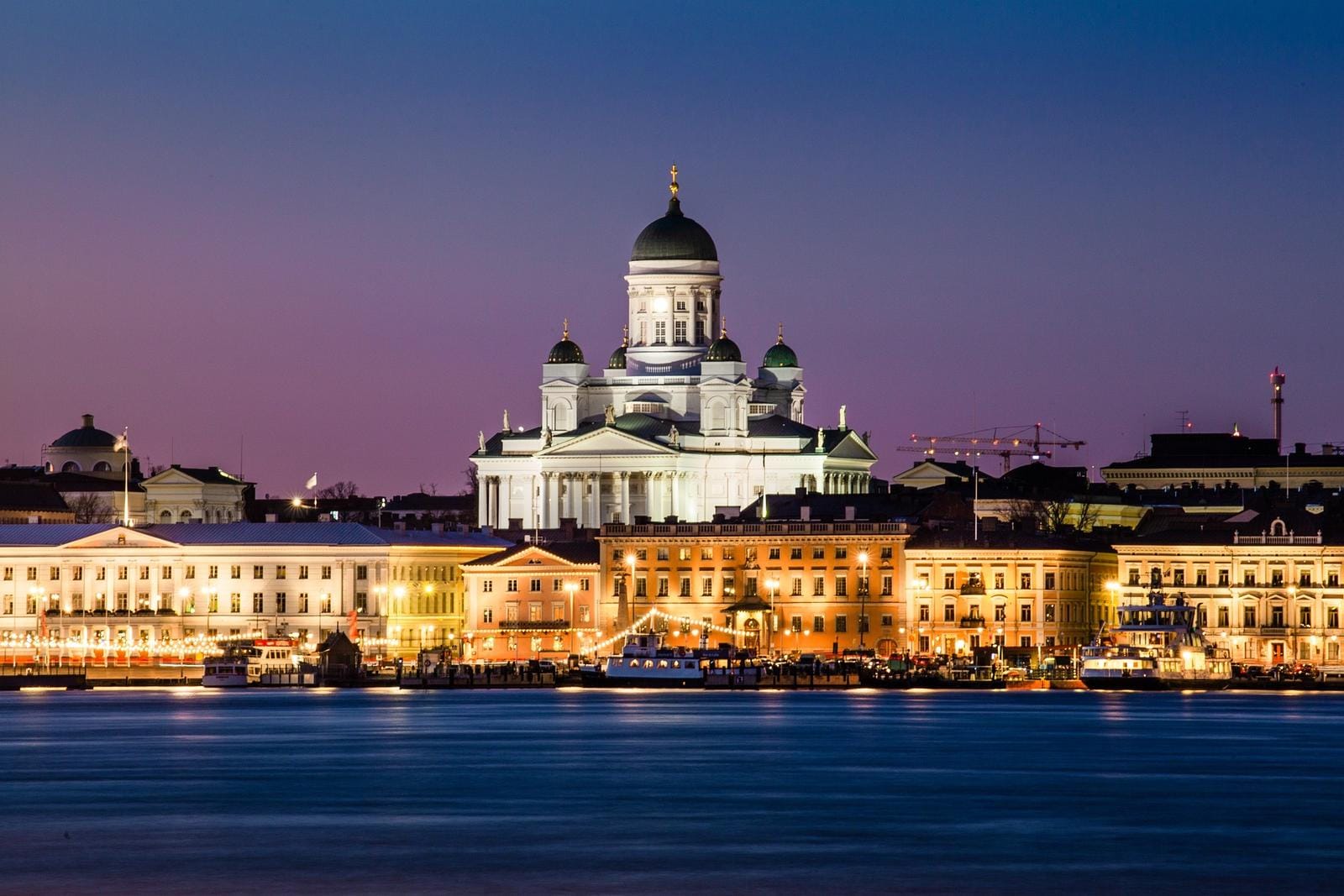 Beleuchtete Kathedrale in Helsinki, Finnland, bei Abenddämmerung, spiegelt sich im ruhigen Wasser.